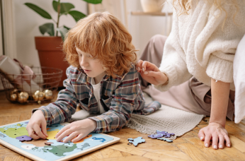 Young child does a puzzle on the floor with an adult nearby, representing support for children with auditory processing disorder.
